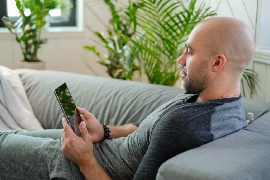 A man lying in a sofa using his phone to get an online Viagra prescription