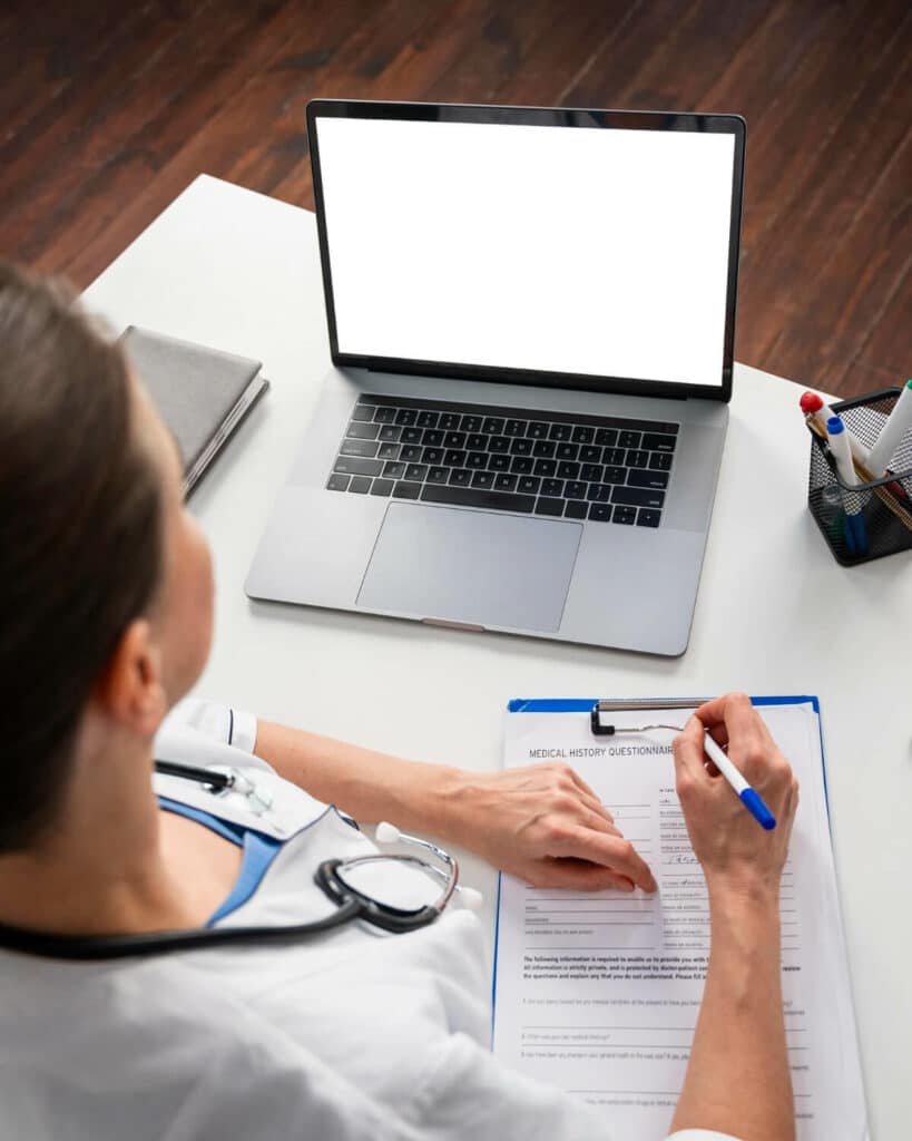 A doctor sitting at her desk filling out a form with a pen in hand to renew a prescription online